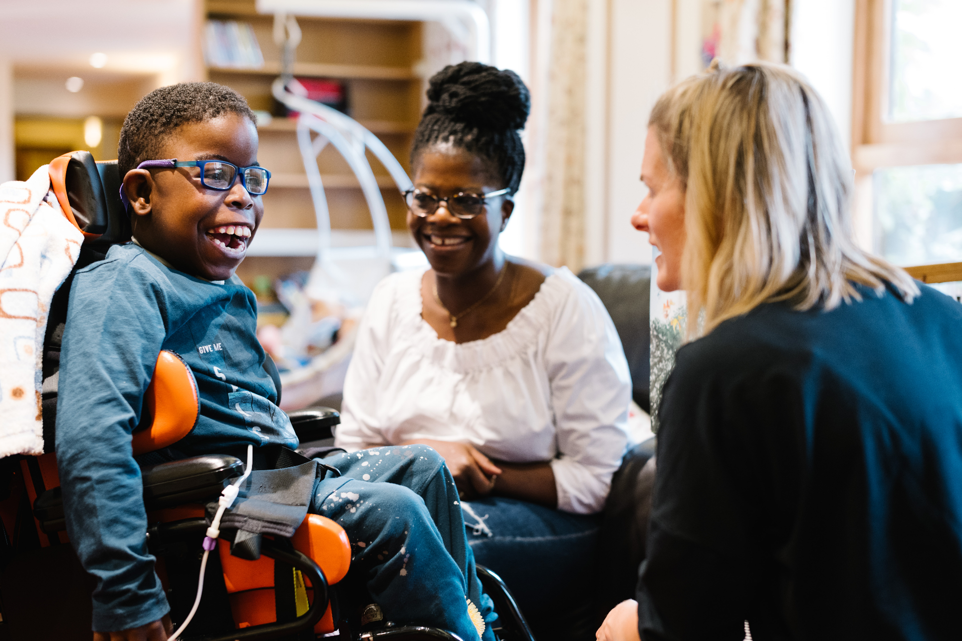 A young boy in a wheelchair laughing with his mother and a hospice worker